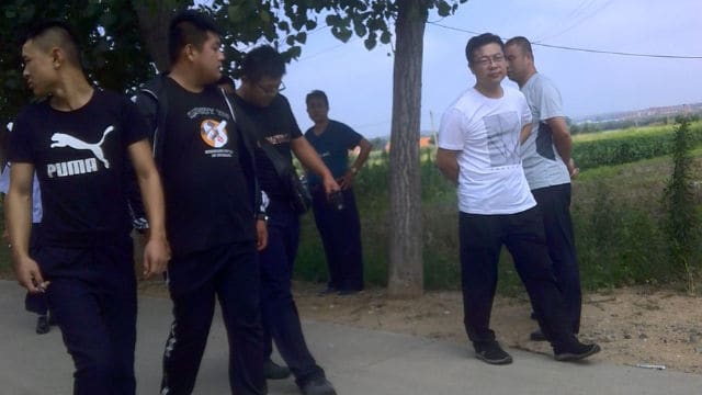 policías vestidos de civil y personal gubernamental se paran frente a la casa de Sun Juchang