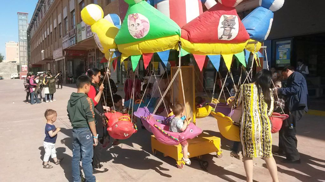 Imágenes contrastantes de Sinkiang: niños jugando en el carrusel contra un trasfondo de "milicias populares" practicando un simulacro en el mercado de Jotán.