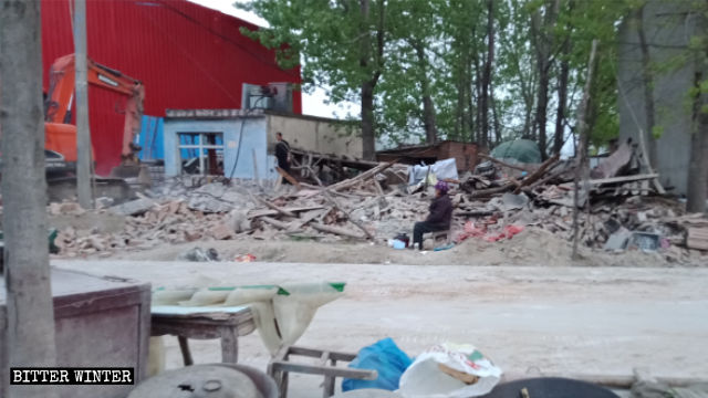 Una mujer mayor sentada junto a las ruinas de su casa demolida en la ciudad de Zhumadian.