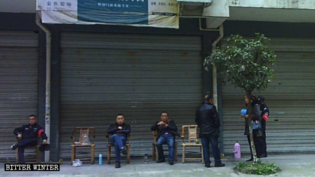 Miembros del personal de la oficina subdistrital vigilan la Iglesia de Qianxiang desde el otro lado de la calle.